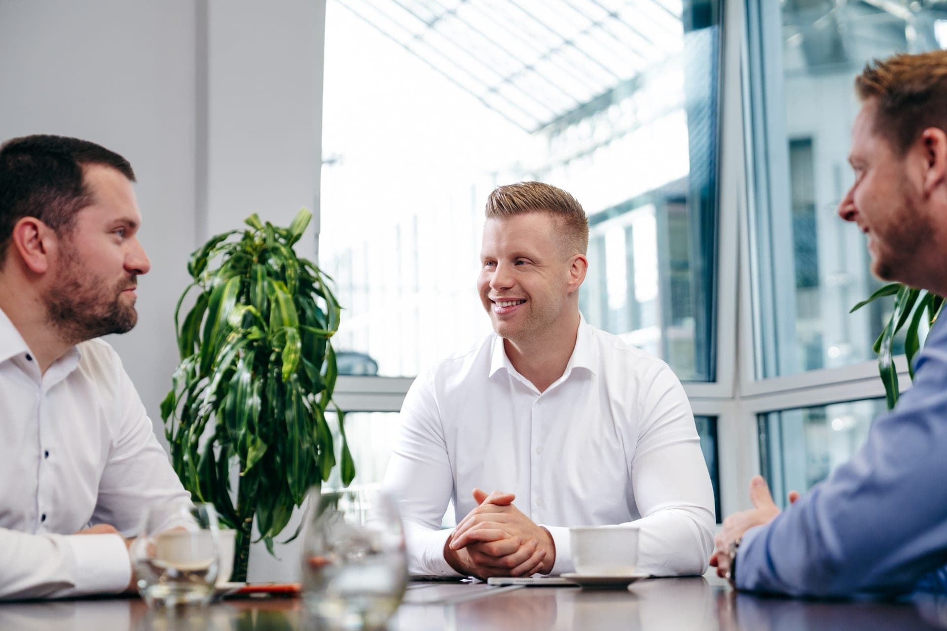 Drei Männer im persönlichen Gespräch an einem Tisch in einem hellen Büro